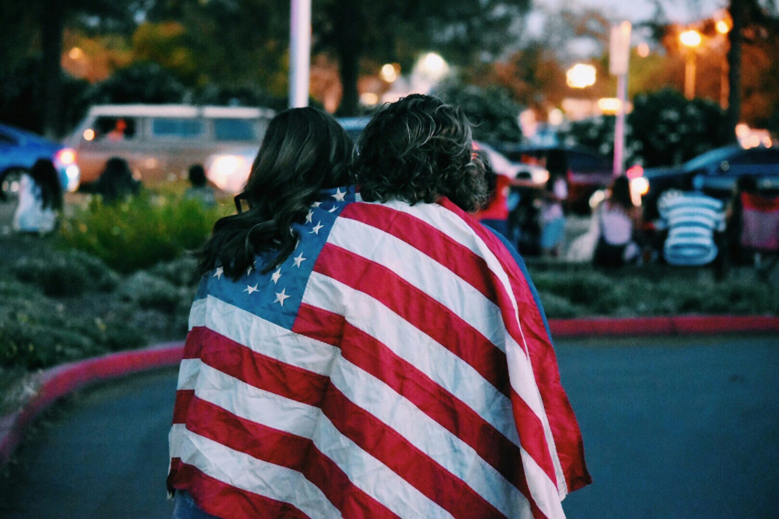 Two women facing street with American flag drapped over their shoulders.