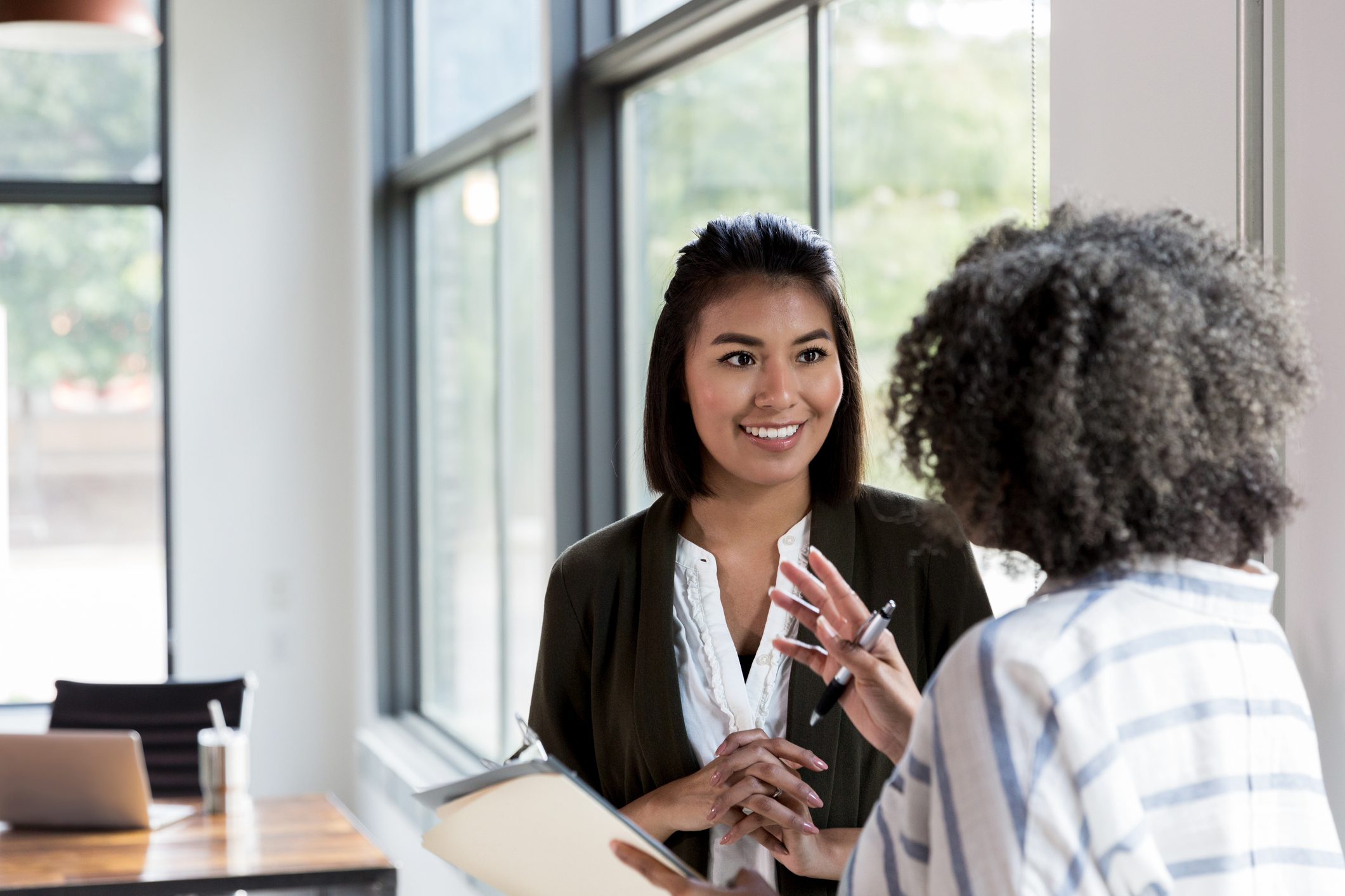 An unrecognizable mature adult female manager gives praise to a smiling mid adult female employee.