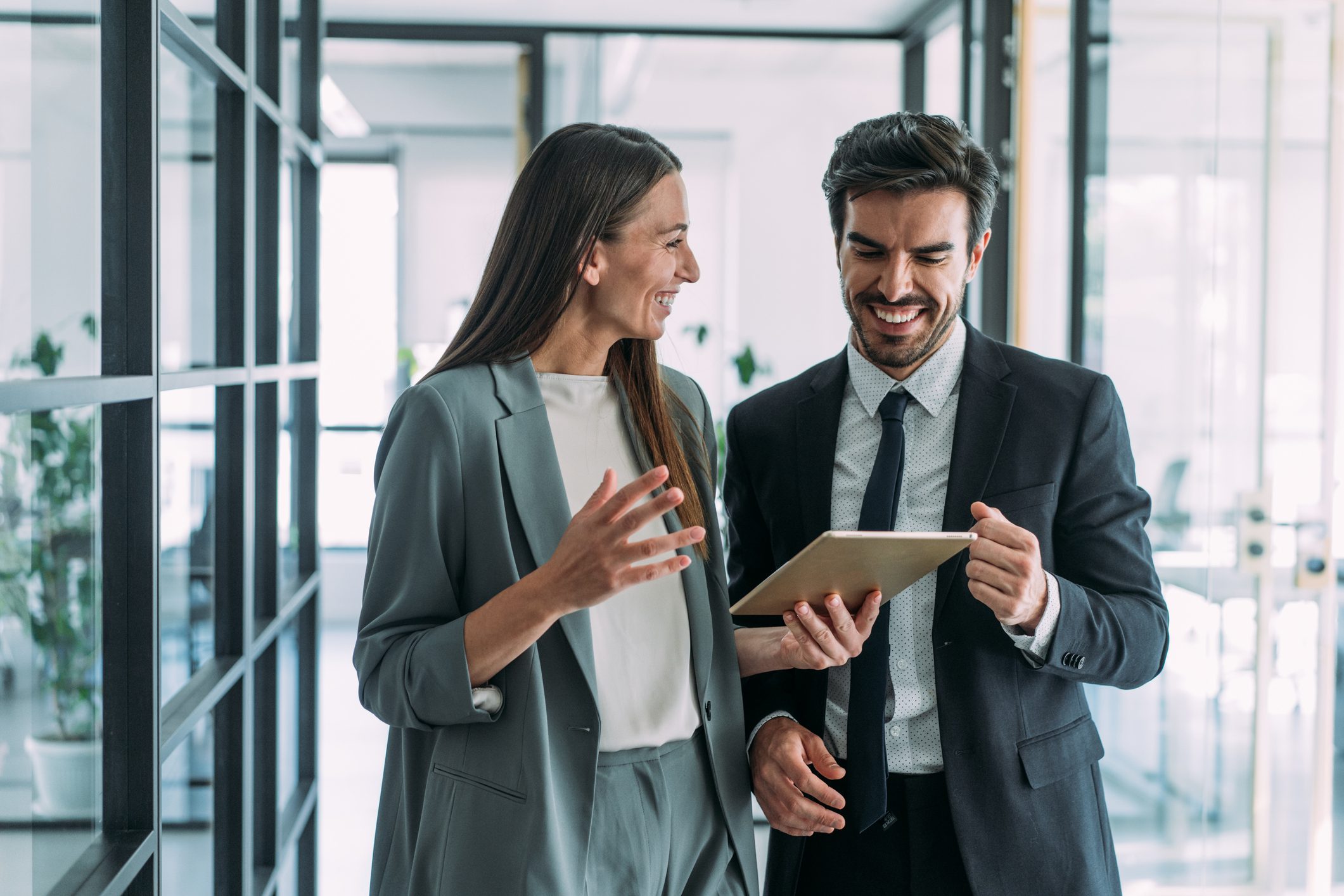 Shot of two coworkers having a discussion in modern office. Businessman and businesswoman in meeting using digital tablet and discussing business strategy. Confident business people working together in the office. Corporate business persons discussing new project and sharing ideas in the workplace.