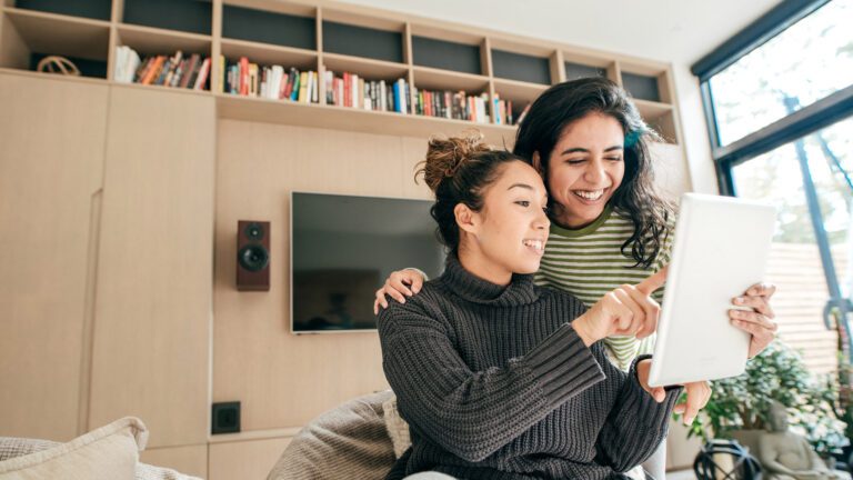 two young women using ipad and smiling