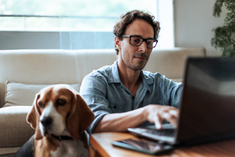 Man sitting with laptop and dog by his side