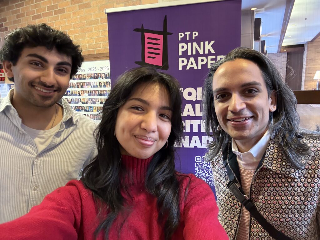 Vijay, Malak and Ronan taking a selfie Infront of the Pink Triangle Press Pink Paper on Health banner